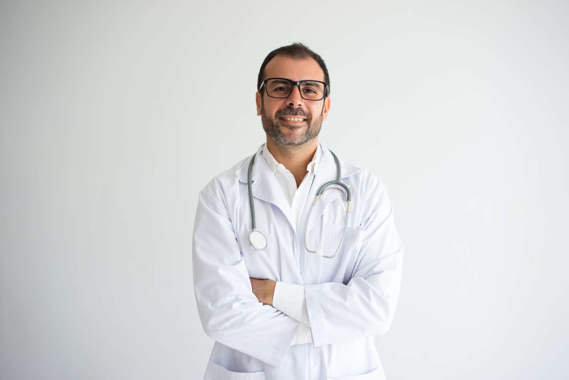 Portrait of successful mid adult doctor with crossed arms. Caucasian general practitioner wearing lab coat, glasses and stethoscope looking at camera and smiling. Medical worker concept